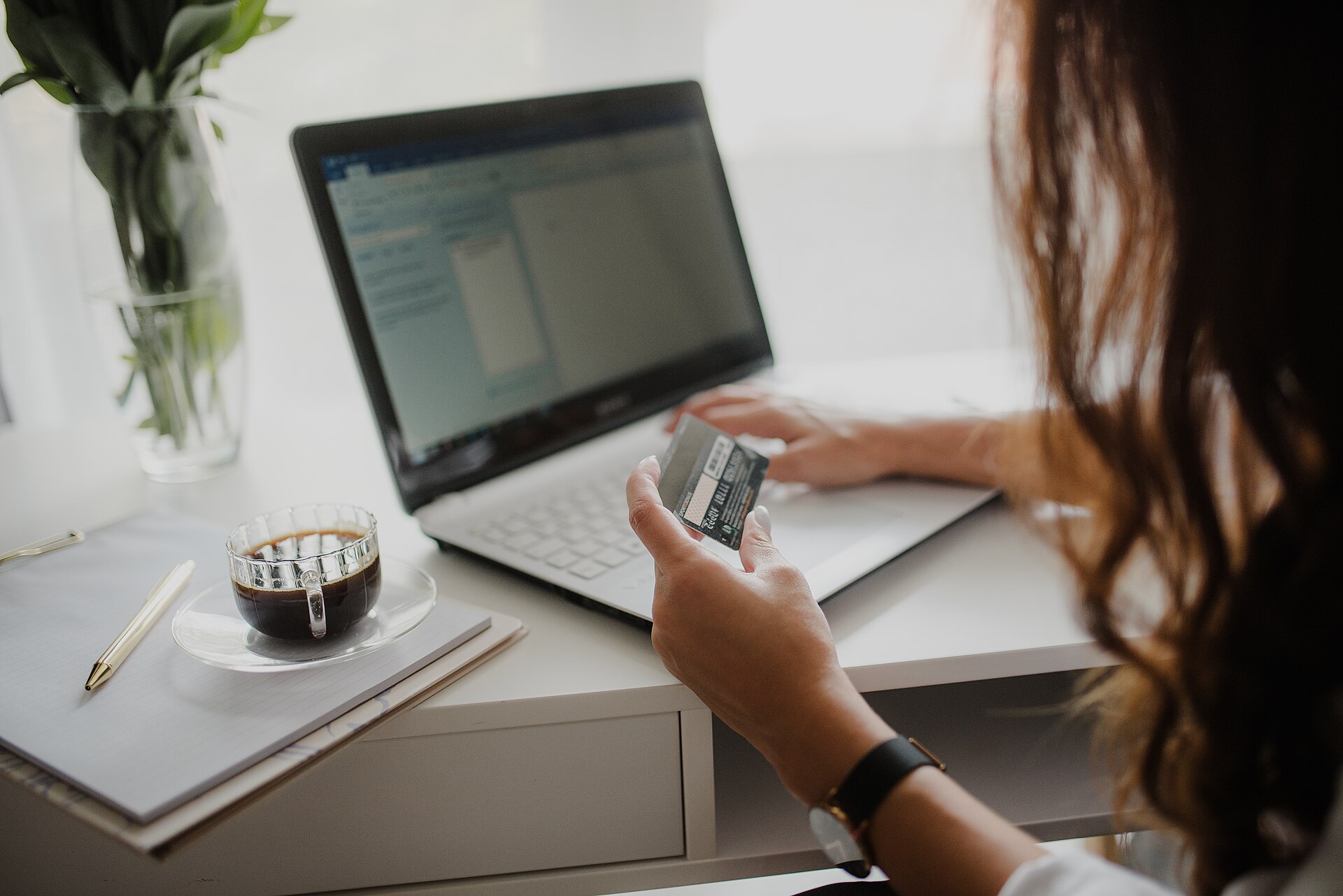 The moment every deal page is written about, and the years afterwards that none of them describe. Photo: Shixart1985, "Close-up of a woman looking at a credit card while working on her laptop", CC BY 2.0, via Wikimedia Commons.